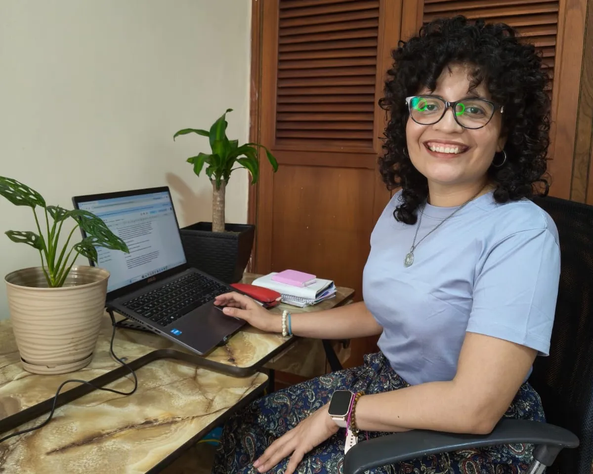 Laimary Linares sonriendo frente a su computadora portátil, en su espacio de trabajo